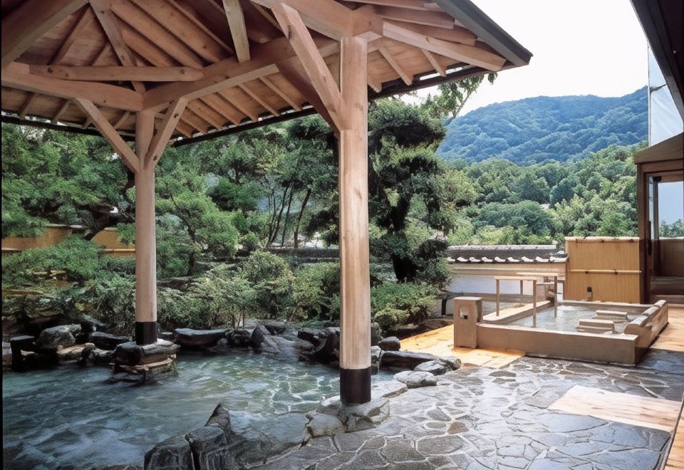 Roofed outdoor bath framed by mountains and trees.