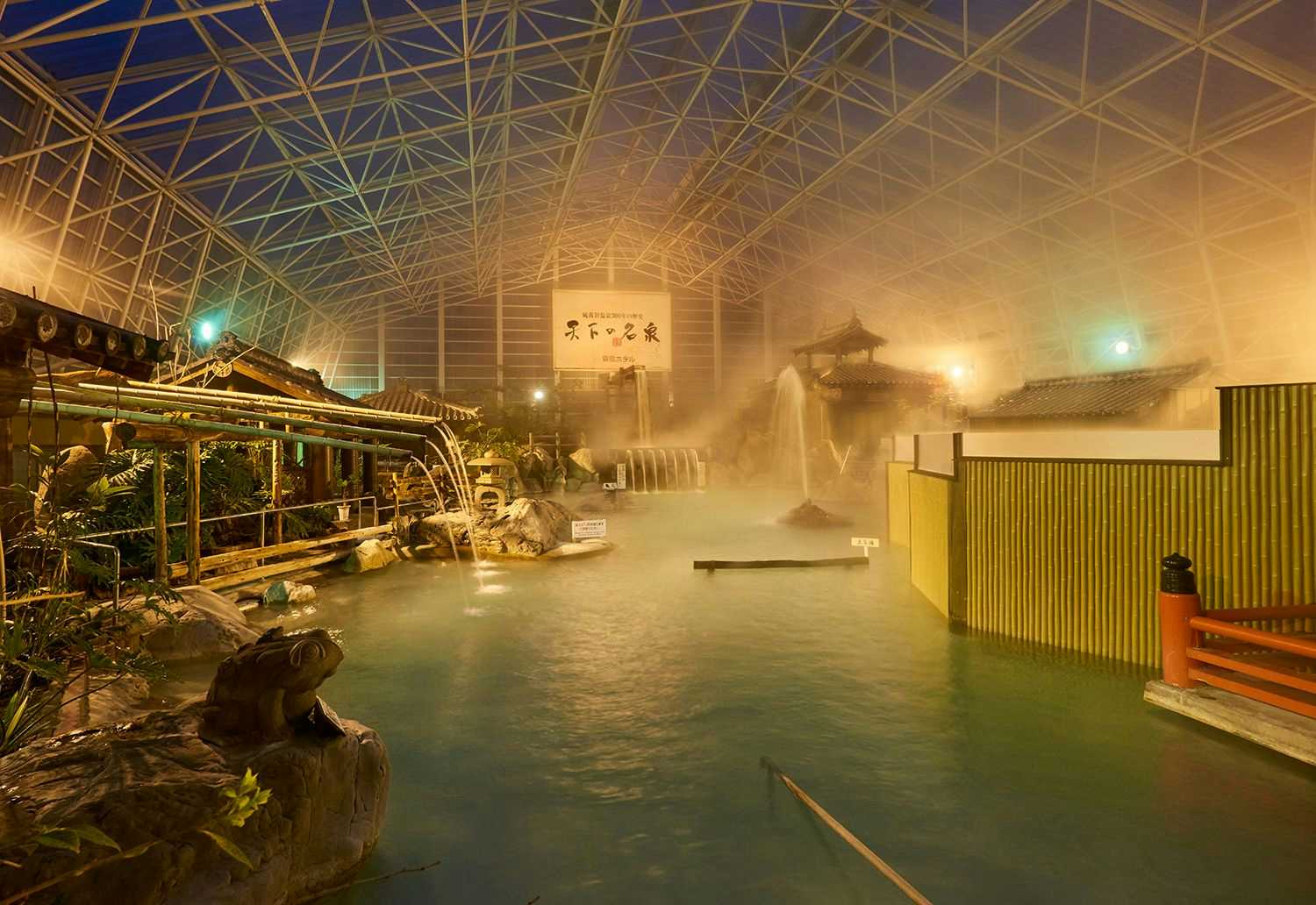 Kirishima Hotel Indoor bath facility with turquoise water, wooden structural elements, glass ceiling, and warm interior lighting.