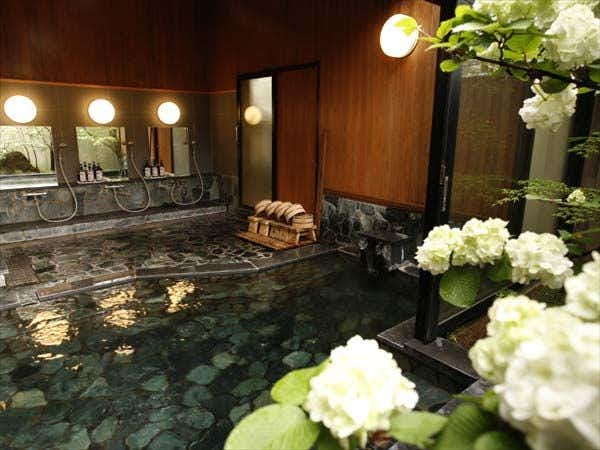Yufuin Onsen Ryokan Hananomai with an indoor stone bath overlooking hydrangeas and garden greenery.