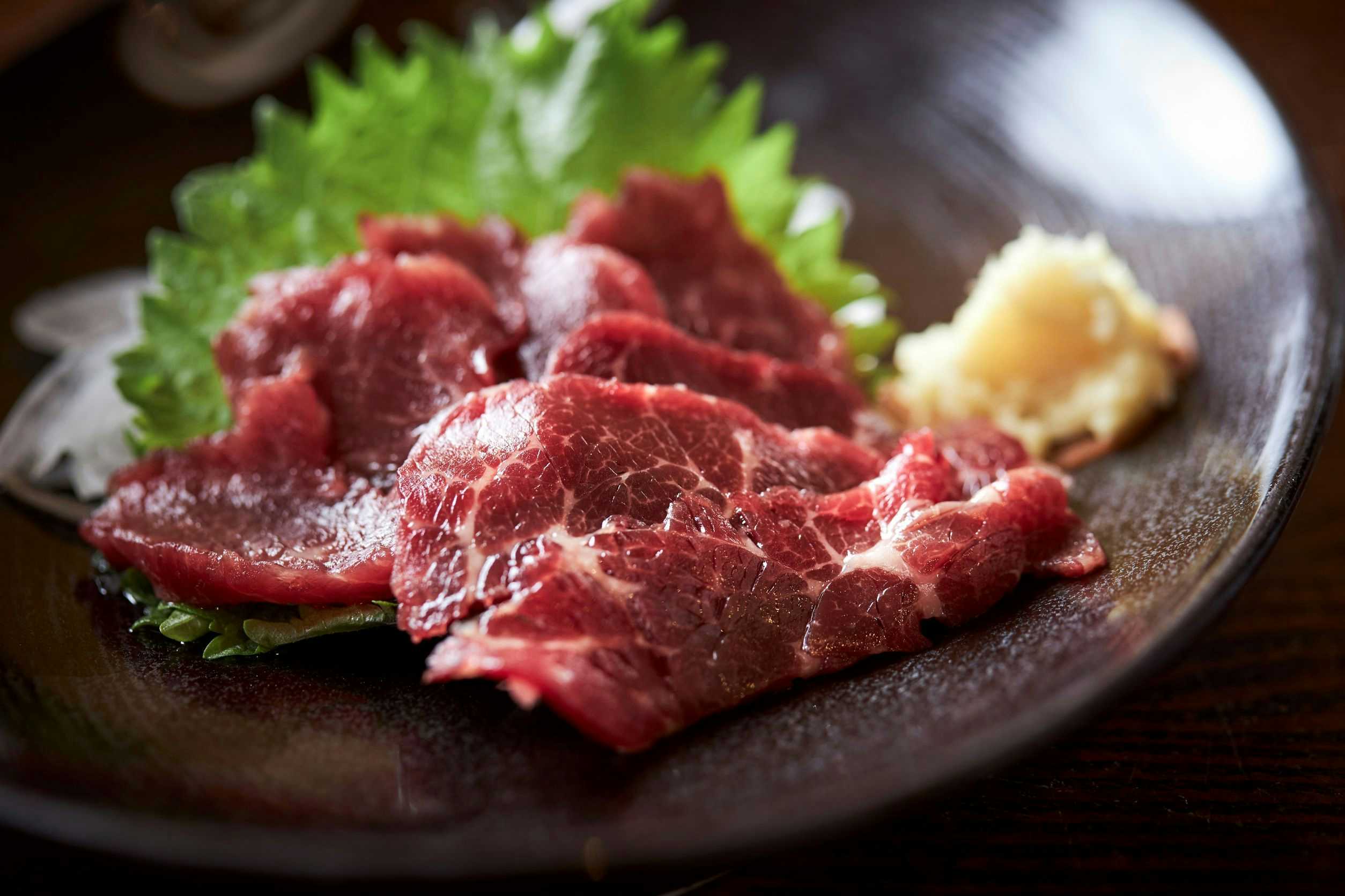 Fumoto Ryokan sliced red meat on dark plate with green herb garnish and sauce elements.