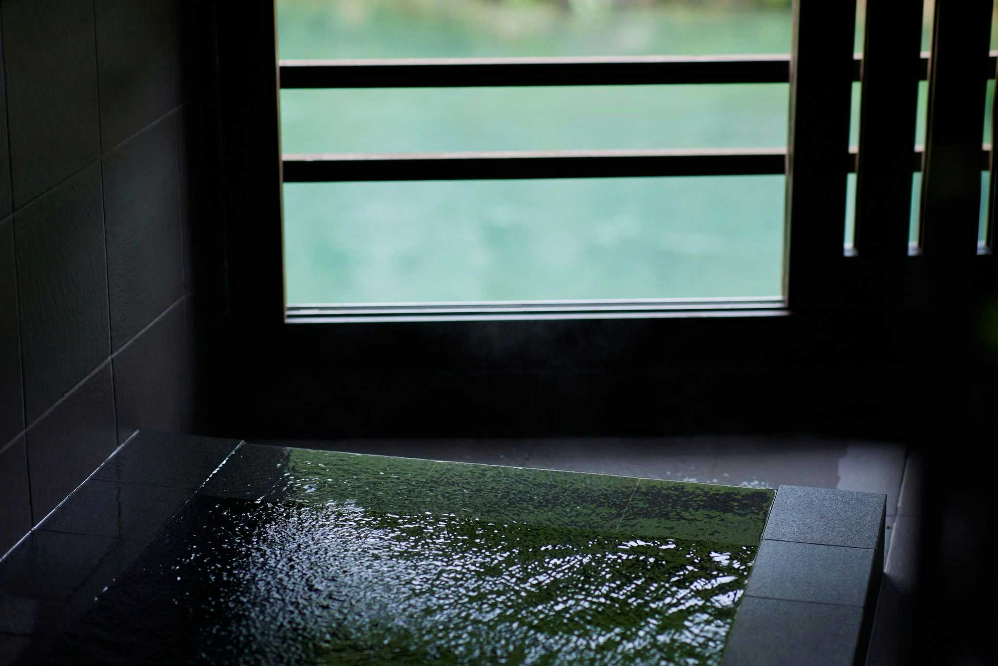 Myoken Onsen Nemu with a private dark stone bath beside narrow river windows.