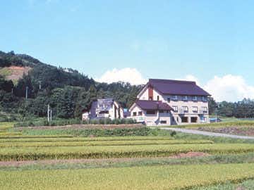 Togari Onsen Shikisai no Yado Kanoe with this scene, where the inn sits beyond open fields in the green Iiyama countryside.