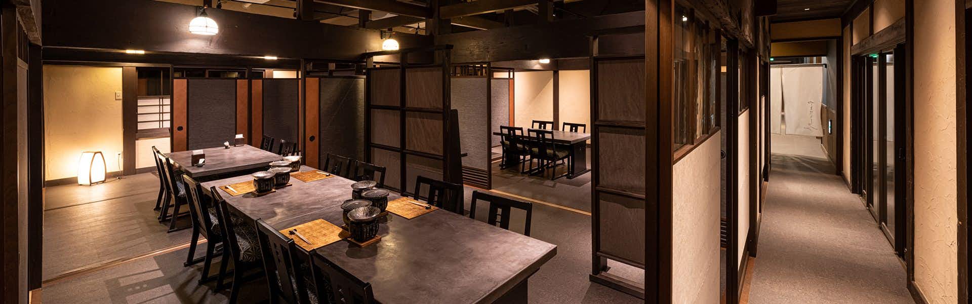 Ryokan Nushiya Wooden table with metal kettle, wooden chairs, latticed partition screens, overhead wooden beams, adjoining seating space