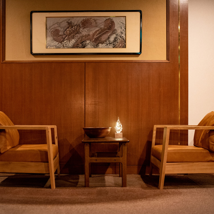 A softly lit lounge features two wooden armchairs beneath framed artwork.
