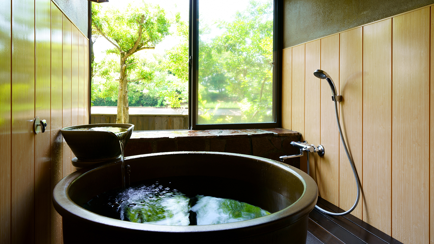 A round tub sits beside a shower and a garden-facing window.