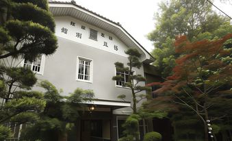 White side facade with Japanese lettering, sash windows, and trimmed trees.