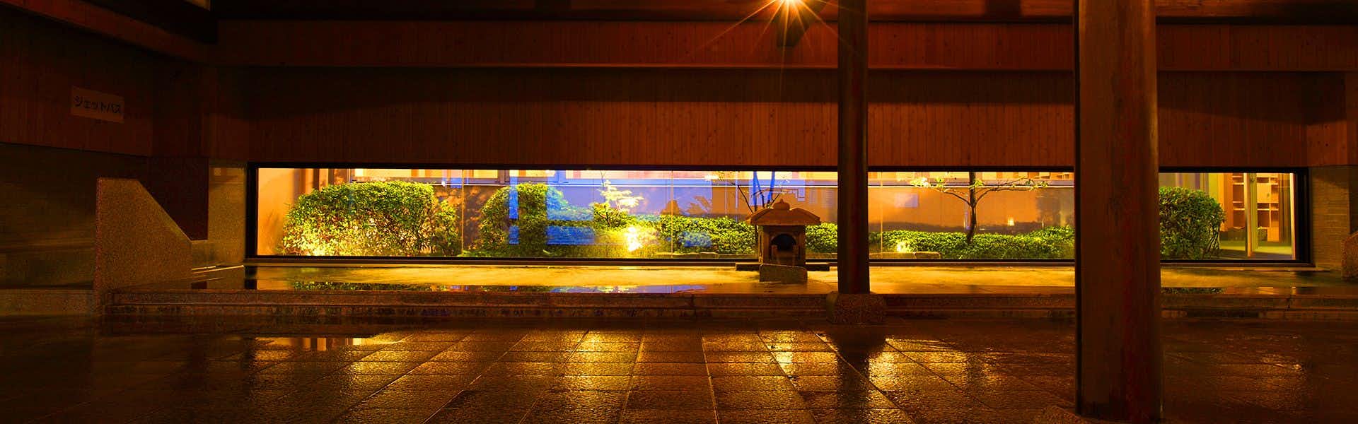Ikaho Onsen Hotel Kogure with a long timber-edged bath glowing beneath panoramic evening windows.