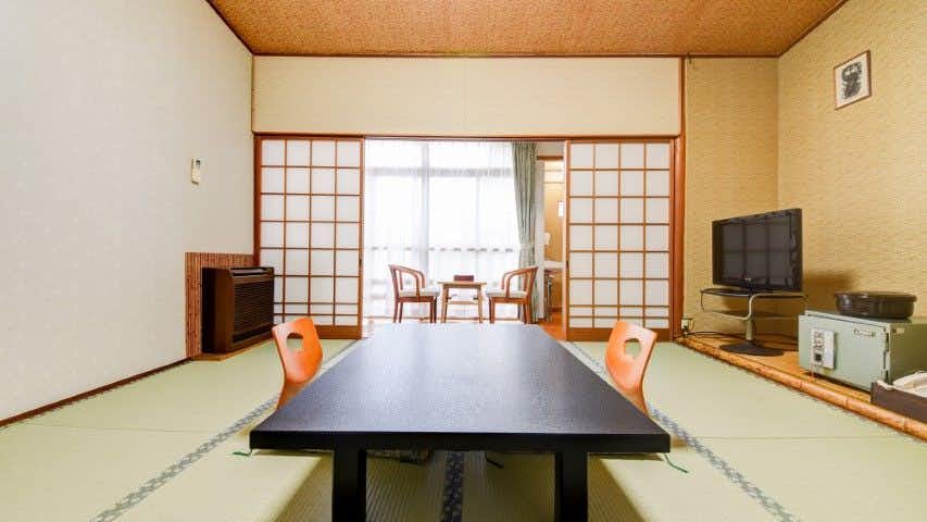 Kawatana Onsen Ryokan Kotengu with this scene, where its tatami guest room centers a black table beside shoji and window seating.