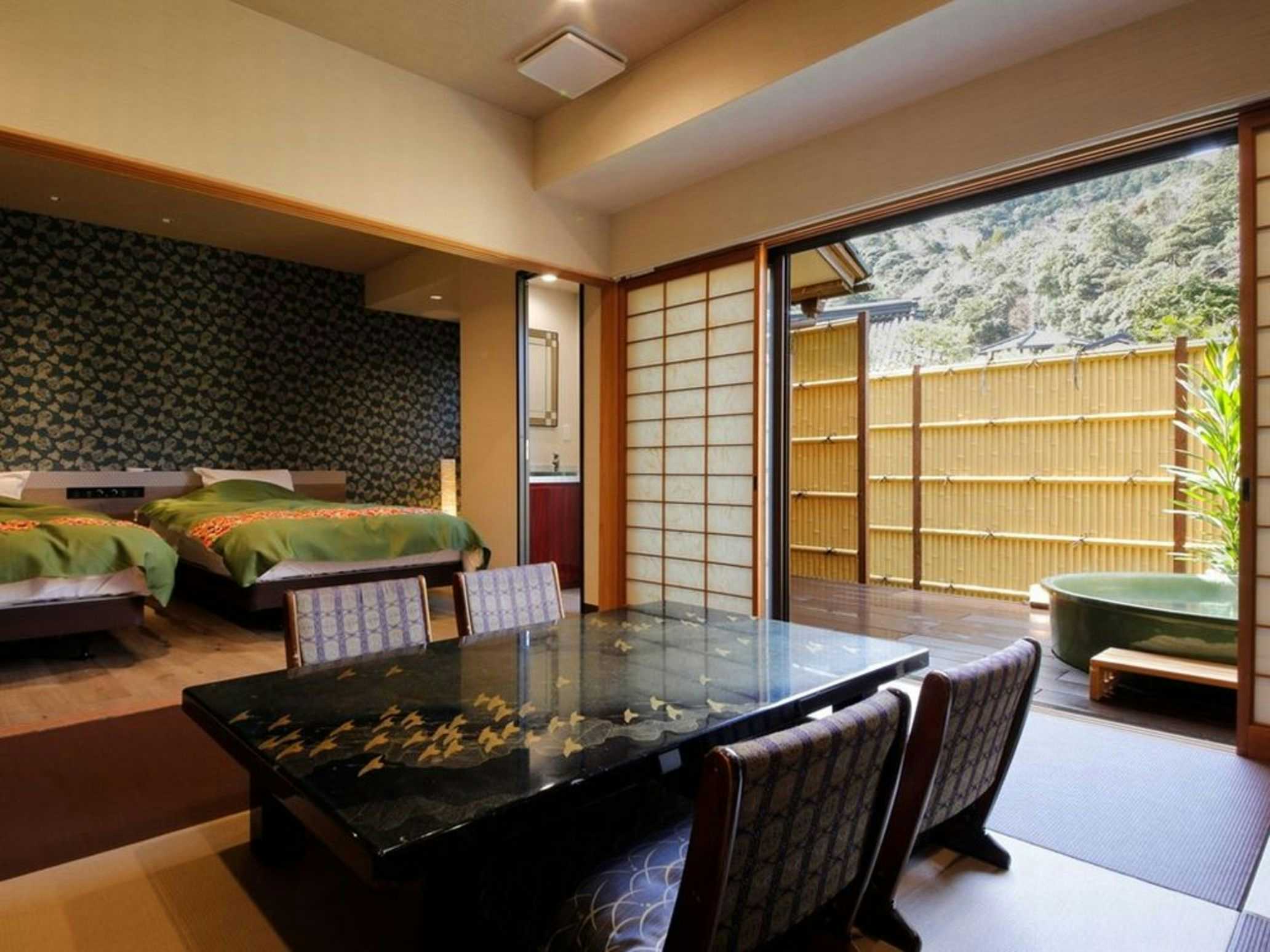 Kinosaki Onsen Hanamandara Interior guest room with wooden low table, sliding door panels showing outdoor greenery, and traditional room furnishings.