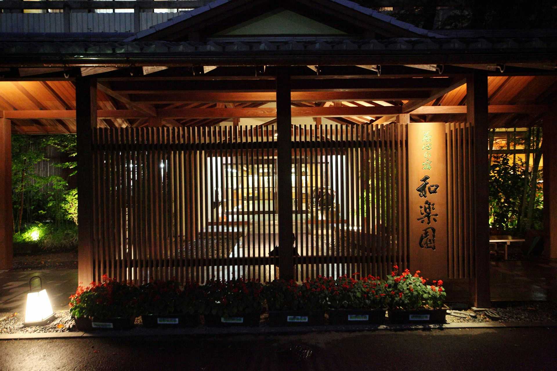 Chagokoro no Yado Warakuen with the timber entrance illuminated behind a flower garden.