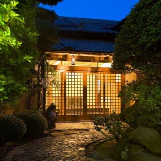 Ryokan Sennari Illuminated wooden lattice entrance with climbing ivy foliage and stone pathway beneath deepening twilight sky.
