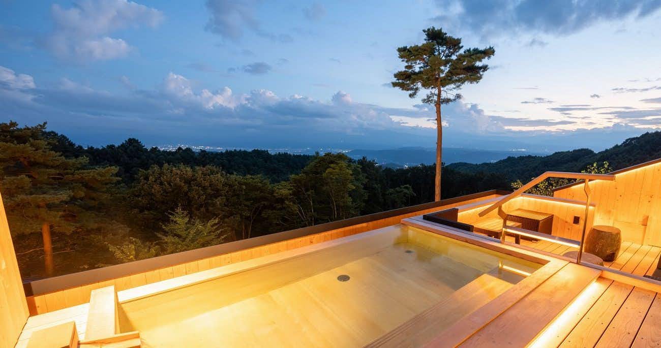 Hishino Onsen Tokiwakan with a private wooden bath facing sunset over distant mountains.