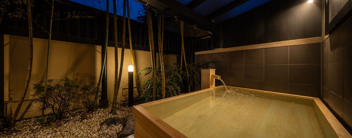 Ritouen a rectangular outdoor wooden bath beside a bamboo screen at night.