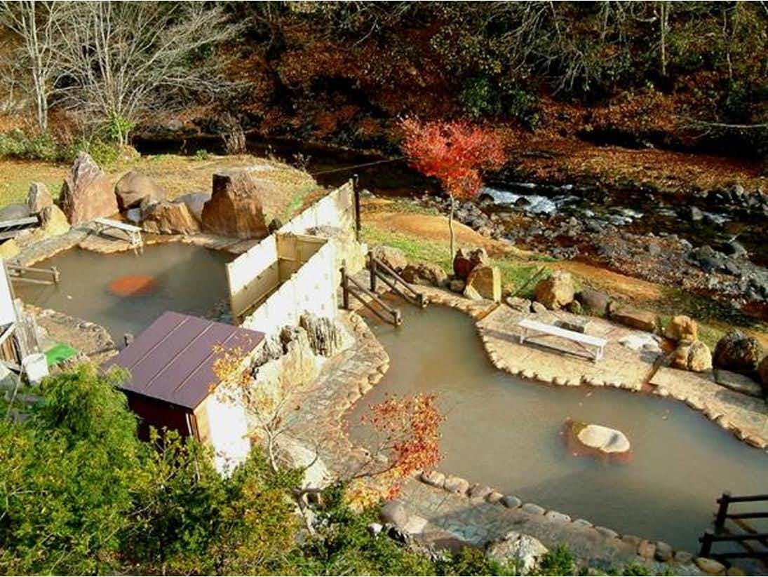 Yakumo Onsen Obokoso with a cluster of outdoor mineral pools beside a forest stream.