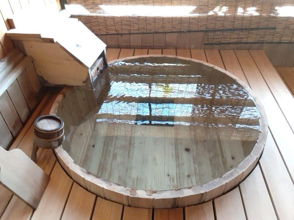 Kusatsu Onsen Yuyado Iwafuji with a round wooden tub, plank floor, window reflections, and a wooden bucket