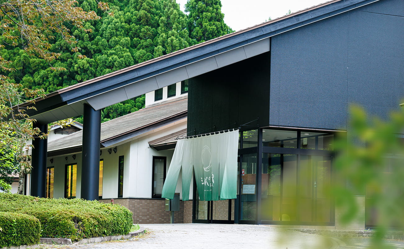 Sanken no Yado Kinomoto angular exterior entrance framed by shrubs and tall green trees