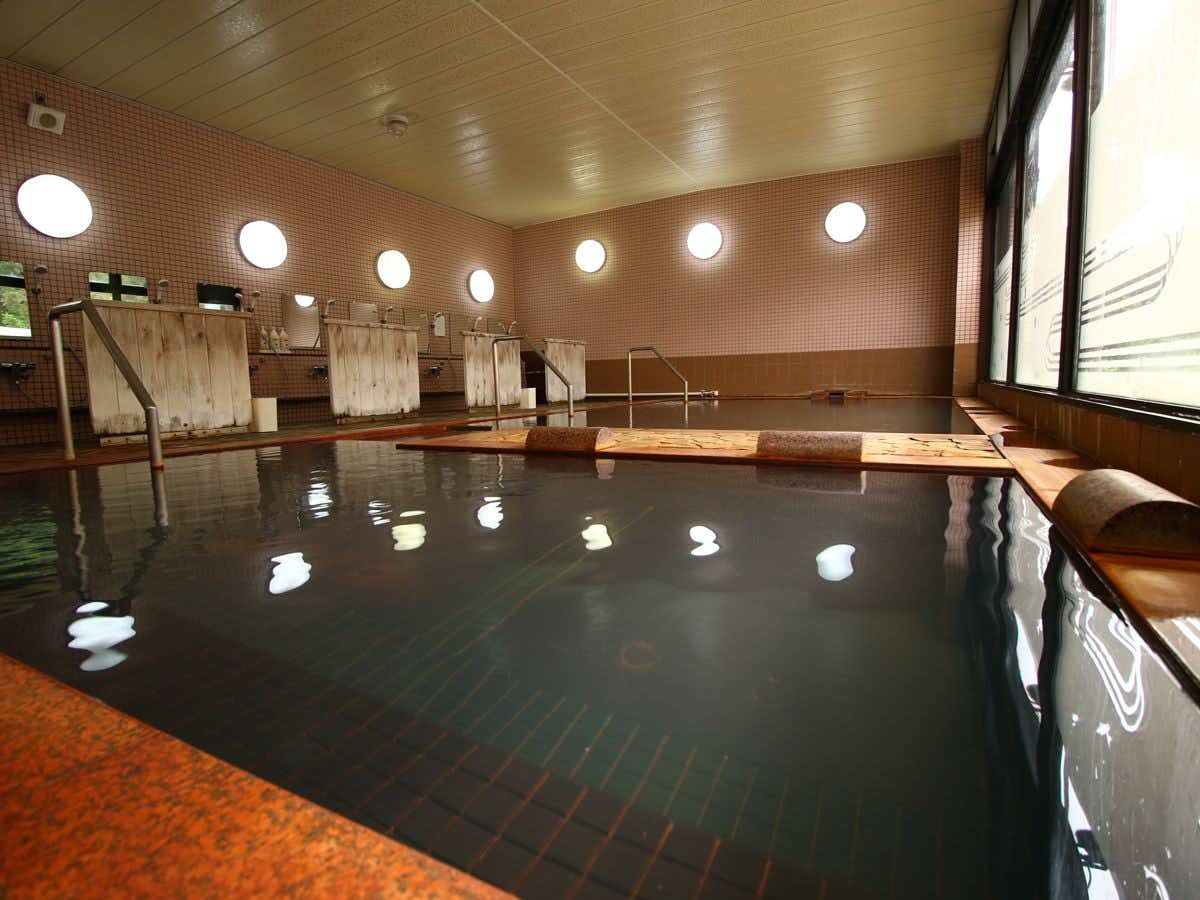 Utto Onsen "Matagi no Yu" with an indoor timber bath beside broad forest windows.