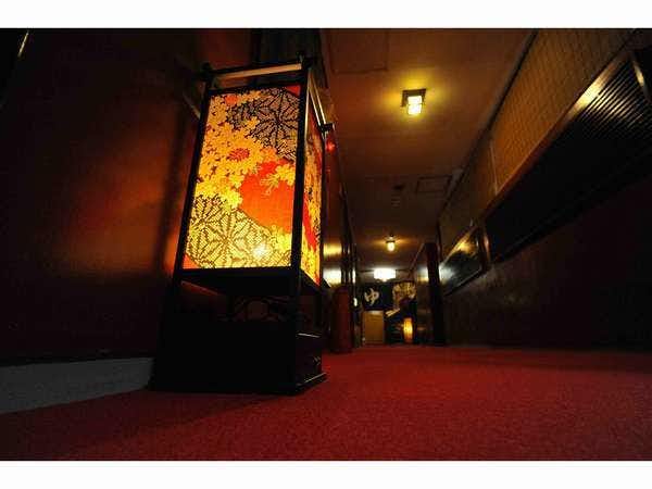 Sakura Kyuan: An Inn with Natural Hot Spring Flow Dim corridor with red carpet, dark wooden walls, warm wall lamps, and a tall illuminated floral lantern