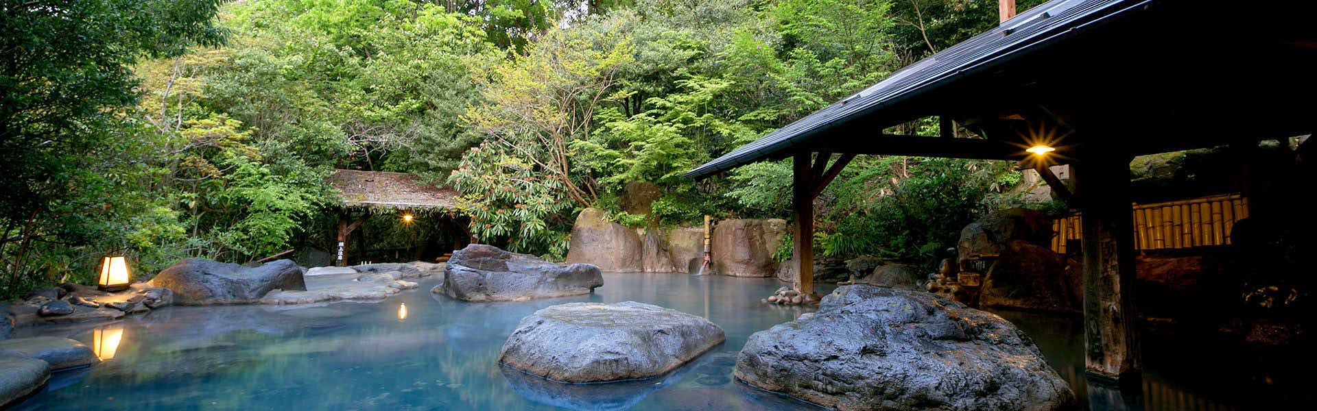 Kurokawa Onsen Yamabiko Ryokan with an open-air rock bath surrounded by leafy forest.