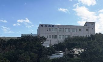 A large white building behind trees beneath a blue sky.