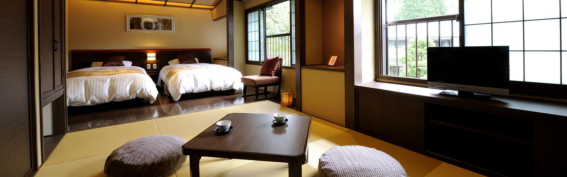 Oyado Ikegami White bedding on dark wood bed frame, side table with ceramic tea service, natural light from windows, tatami-style flooring, wooden furniture.
