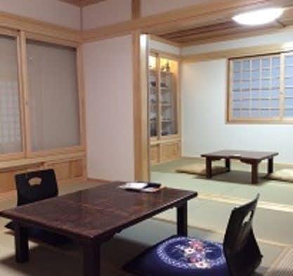 Horieya Ryokan Interior space with dark wooden table, black chair, light wood sliding doors, beige tatami flooring section, fluorescent ceiling light.