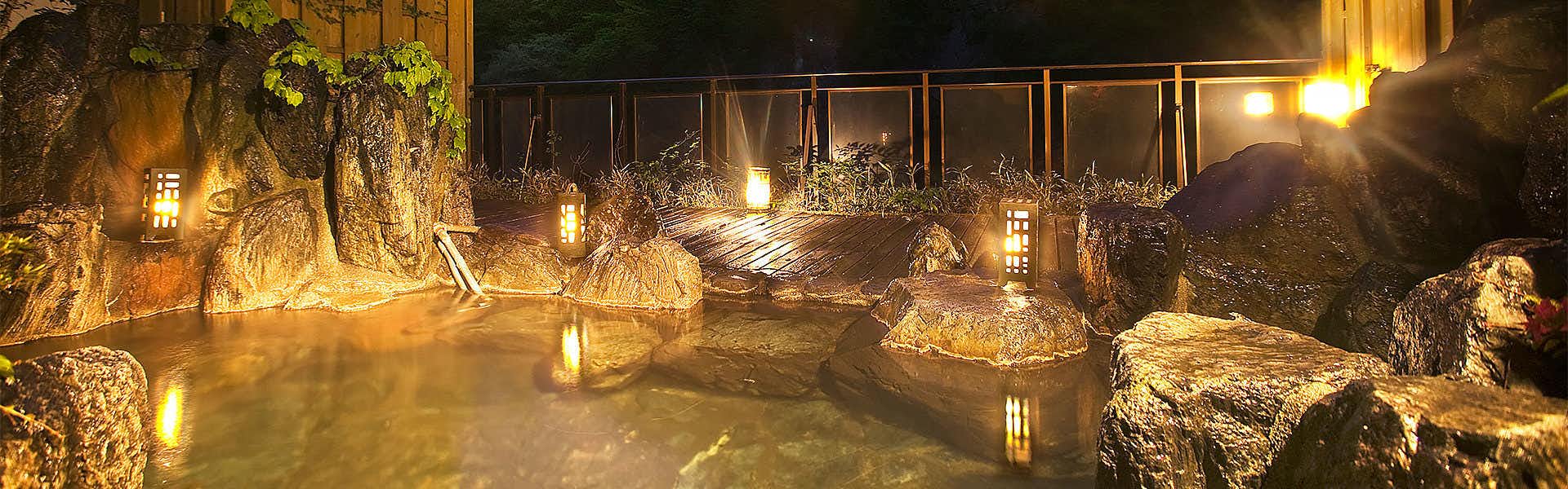 Shiobara Onsen Hito-Toki-Omoi wo Tsumugu Yado Ayatsumugi with lantern-lit outdoor baths surrounded by rocks and dark foliage.