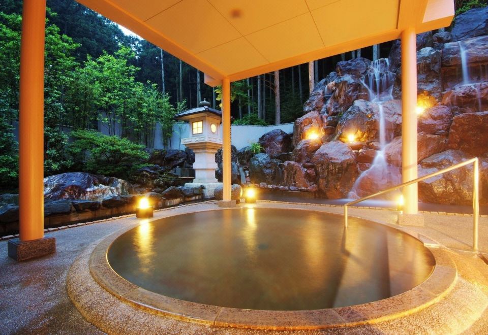 A round outdoor bath beside a rock waterfall.