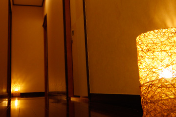 A glowing woven floor lamp in a wooden corridor.