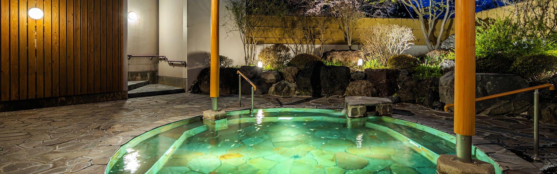 Gensen-yu no Yado Shisuitei with an open-air stone bath glowing green beside garden rocks.