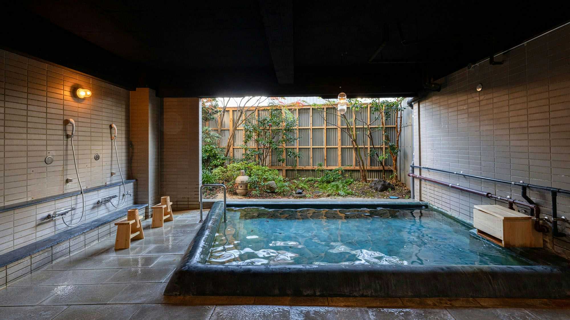 Nisaino Yuyado Asahiya Large rectangular indoor bath with dark tile surround, washing stations, open garden view, and wooden stools and buckets