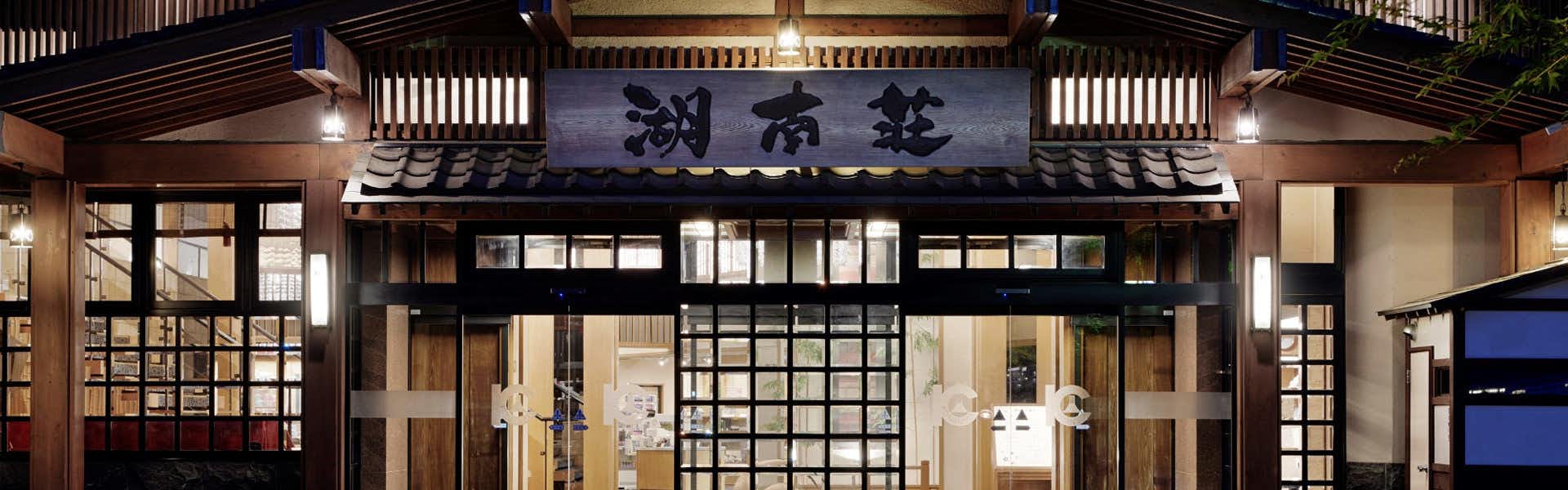 Fujikawaguchiko Onsen Konanso with an illuminated timber entrance with white noren at night.