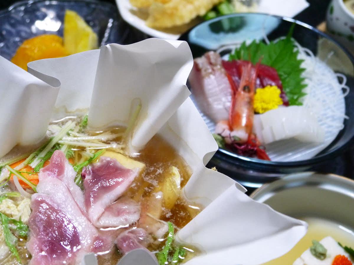 Hasedera Yumoto Itaniya with this scene, where thin slices of meat and vegetables simmer in white paper beside a small sashimi plate.