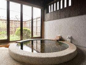 Aso no Tabiyado Takanosho with a round stone soaking tub beside tall garden windows.