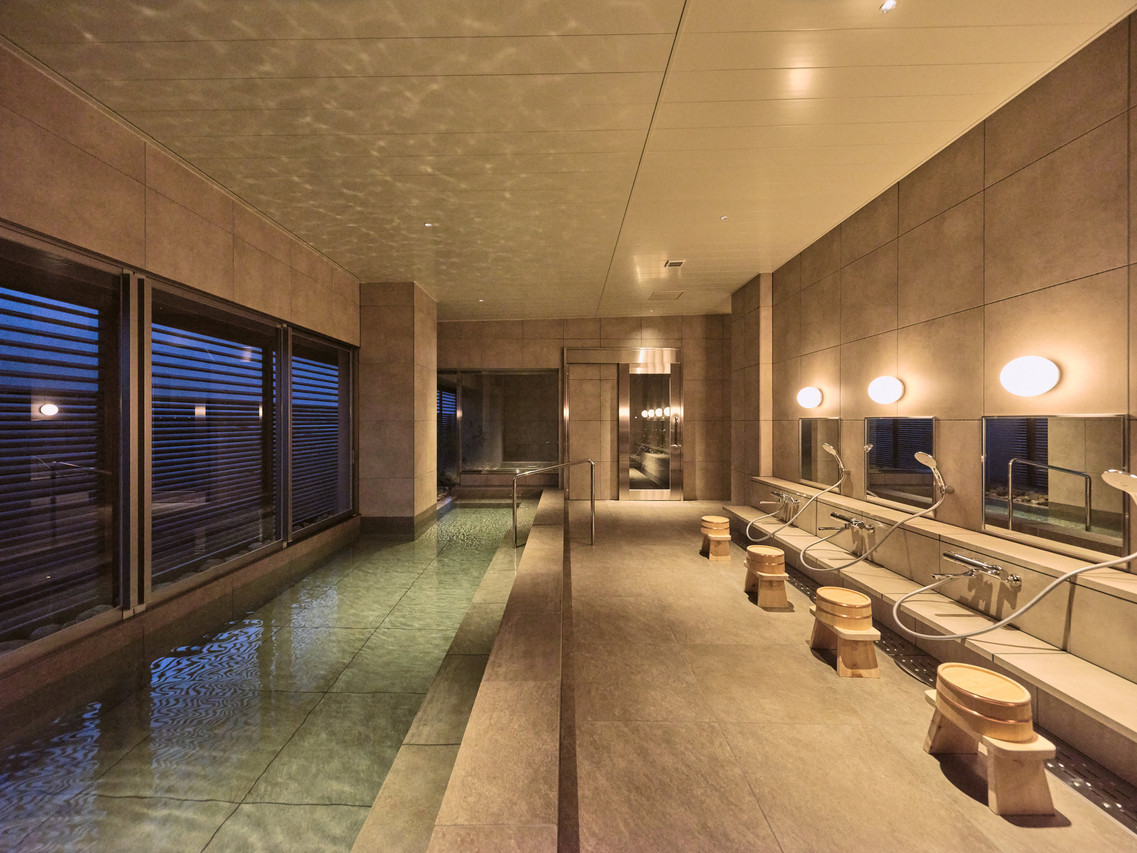 Indoor bathing area with tiled pools and round stools.