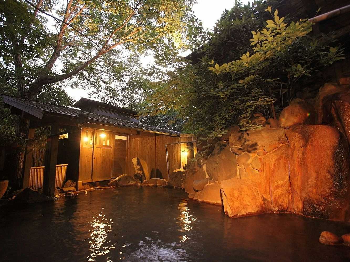 Ryokan Yamanoyu with an outdoor bath glowing beside natural rock walls at night.