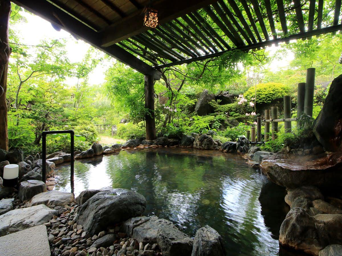 Shinkashi Onsen Gohousou with an outdoor rock bath beneath a leafy timber canopy.