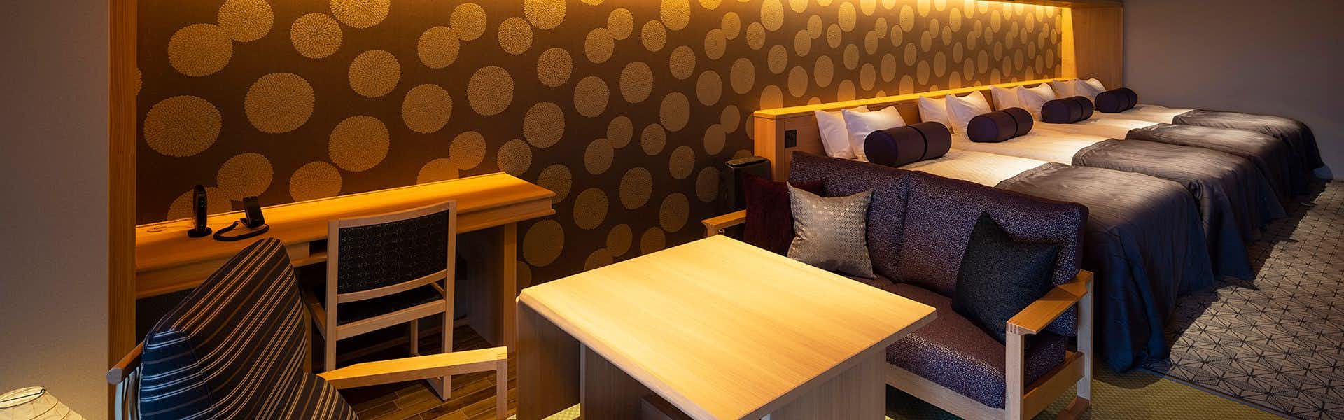 Yumoto Konpira Onsen Hananoyu Koubaitei Cream-colored counter with beds featuring dark bedding visible beyond, decorative seating, and warm amber lighting.