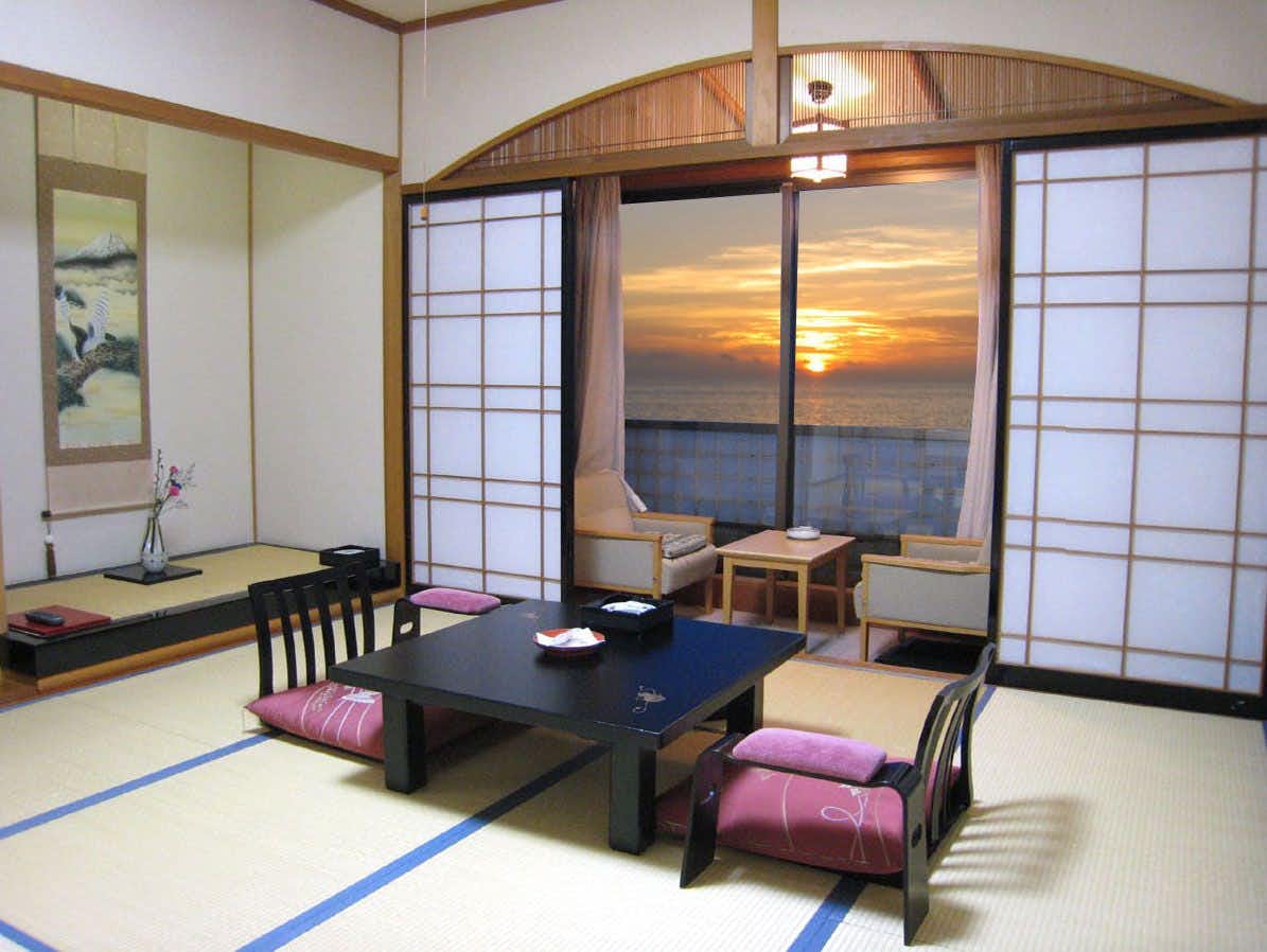 Hotel Kappo Ishimaru: The Inn of Echizen Crab and Natural Abalone Tatami room with low black table, floor chairs, paper screens, and a window framing sunset over open water