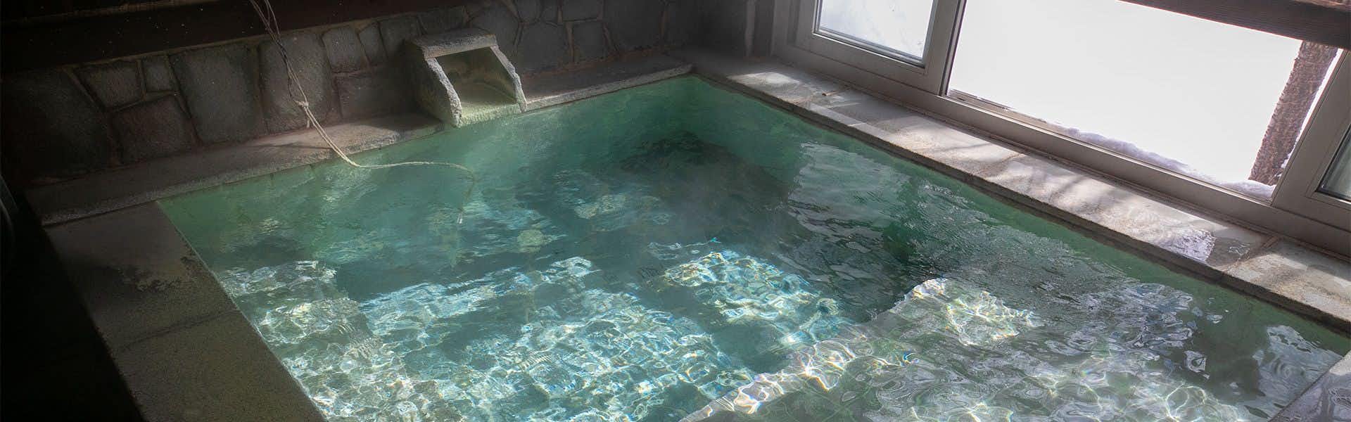 Gokan no Yu Tsuruy pool area with turquoise water, visible rocky bottom pattern, and right-side window