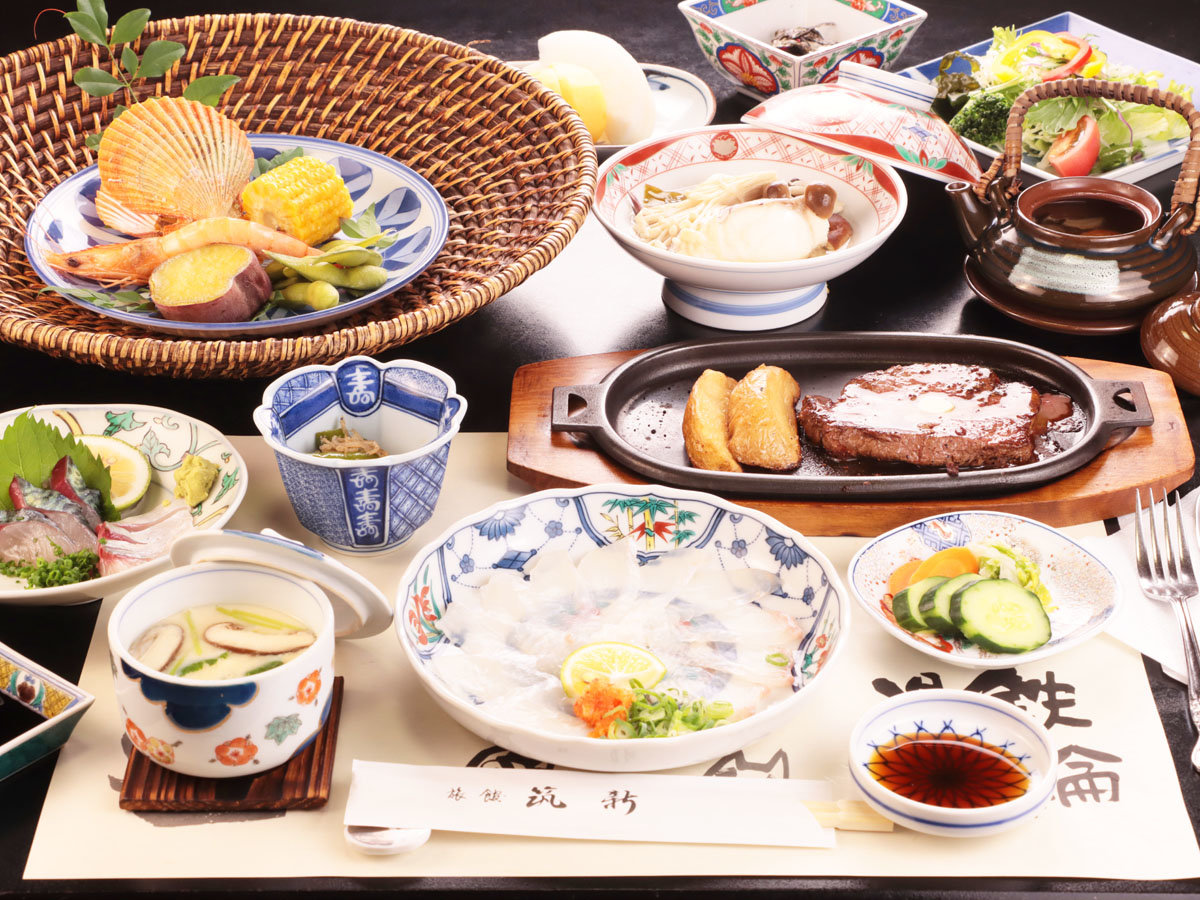 A Japanese meal is arranged across patterned dishes beside a hot plate.