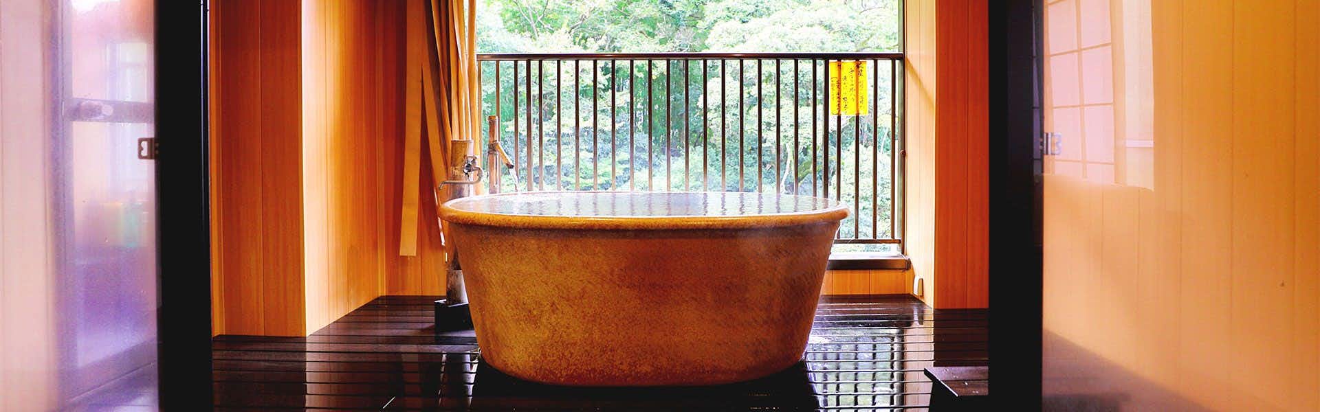 Mizu no Michi Kaze no Michi Yugashima Tatsuta copper-toned soaking tub beside window framed in orange wood with wooden platform flooring