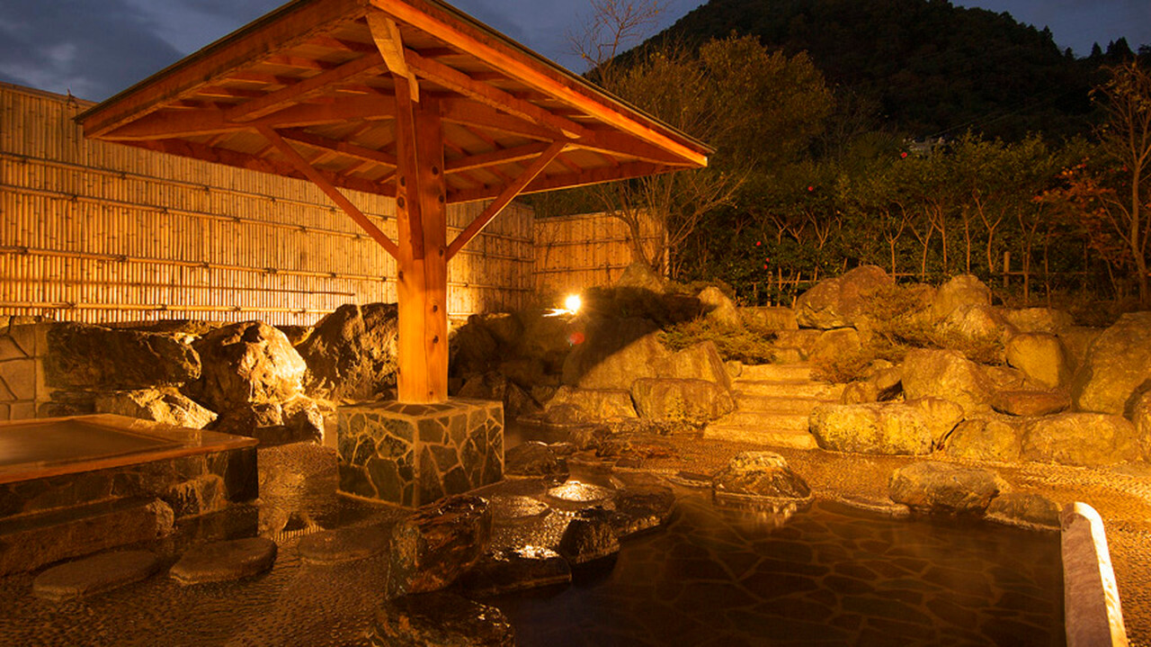 A covered outdoor bath is surrounded by rocks and trees.