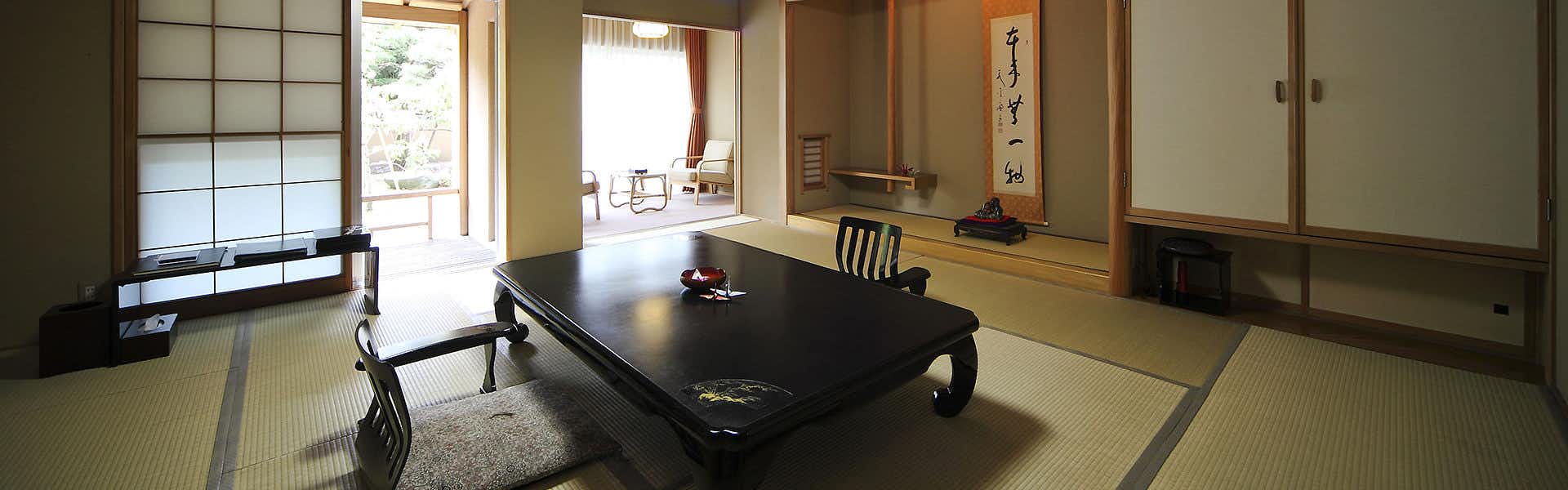 Tabist Chikuba Shinyotei Hakodate Yunokawa Onsen Room with woven natural-fiber flooring, low dark table, furnishings, and window with geometric lattice pattern.