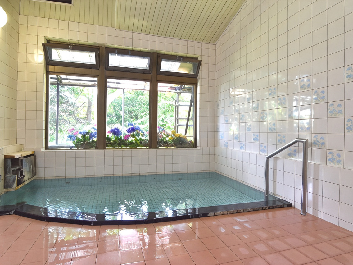 A tiled bath sits beside windows overlooking flowering shrubs.