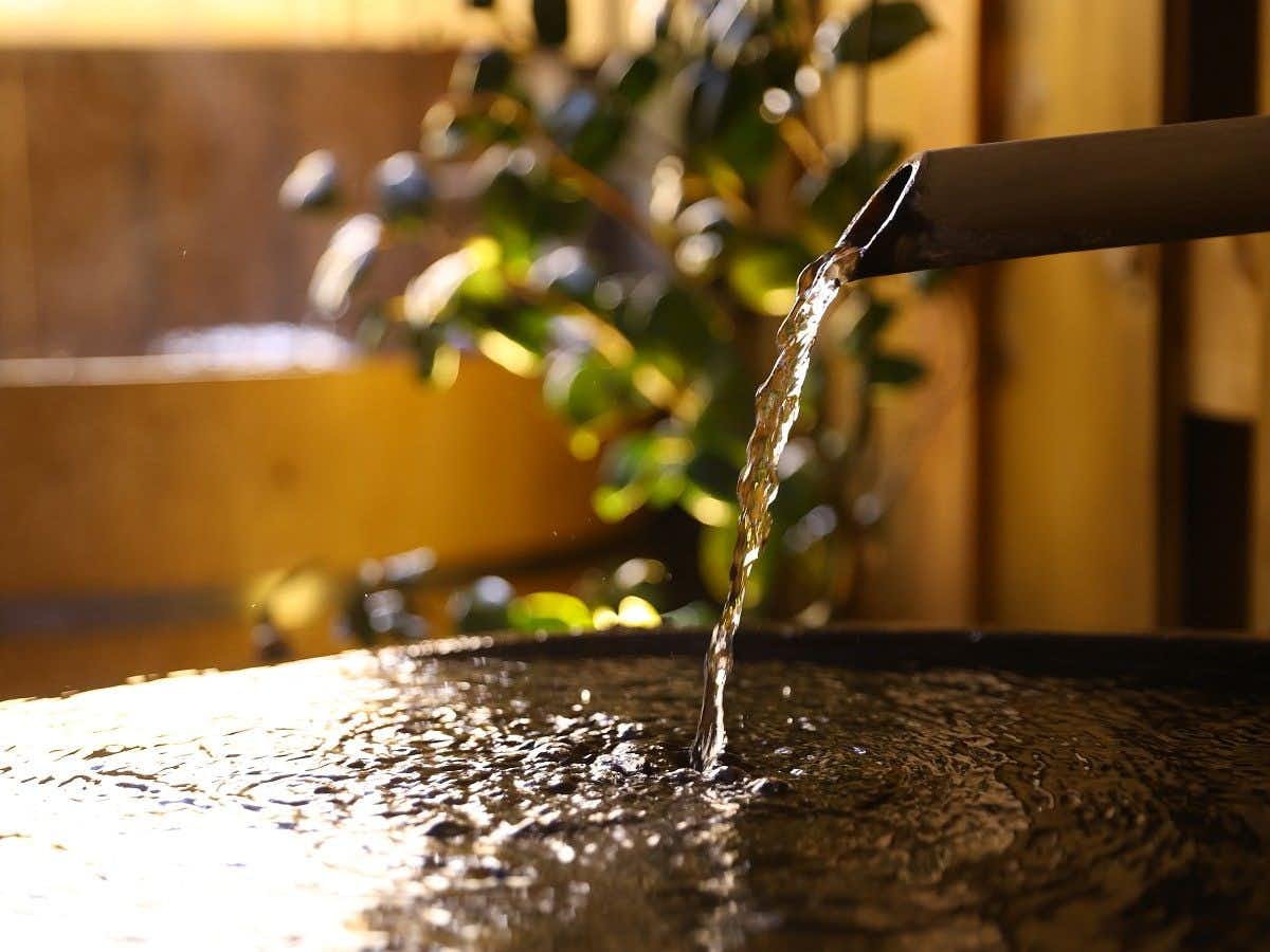 Kakeyu Onsen Kuroiwa Ryokan with this scene, where fresh onsen water pours from a dark spout into a tiled bath.