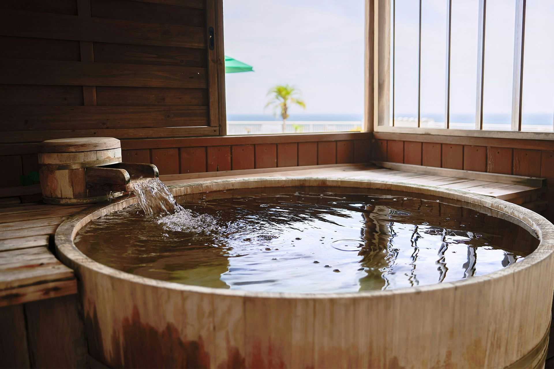 Atami no Yu Shinkadoya round wooden bath beside broad windows facing the sea and a palm tree