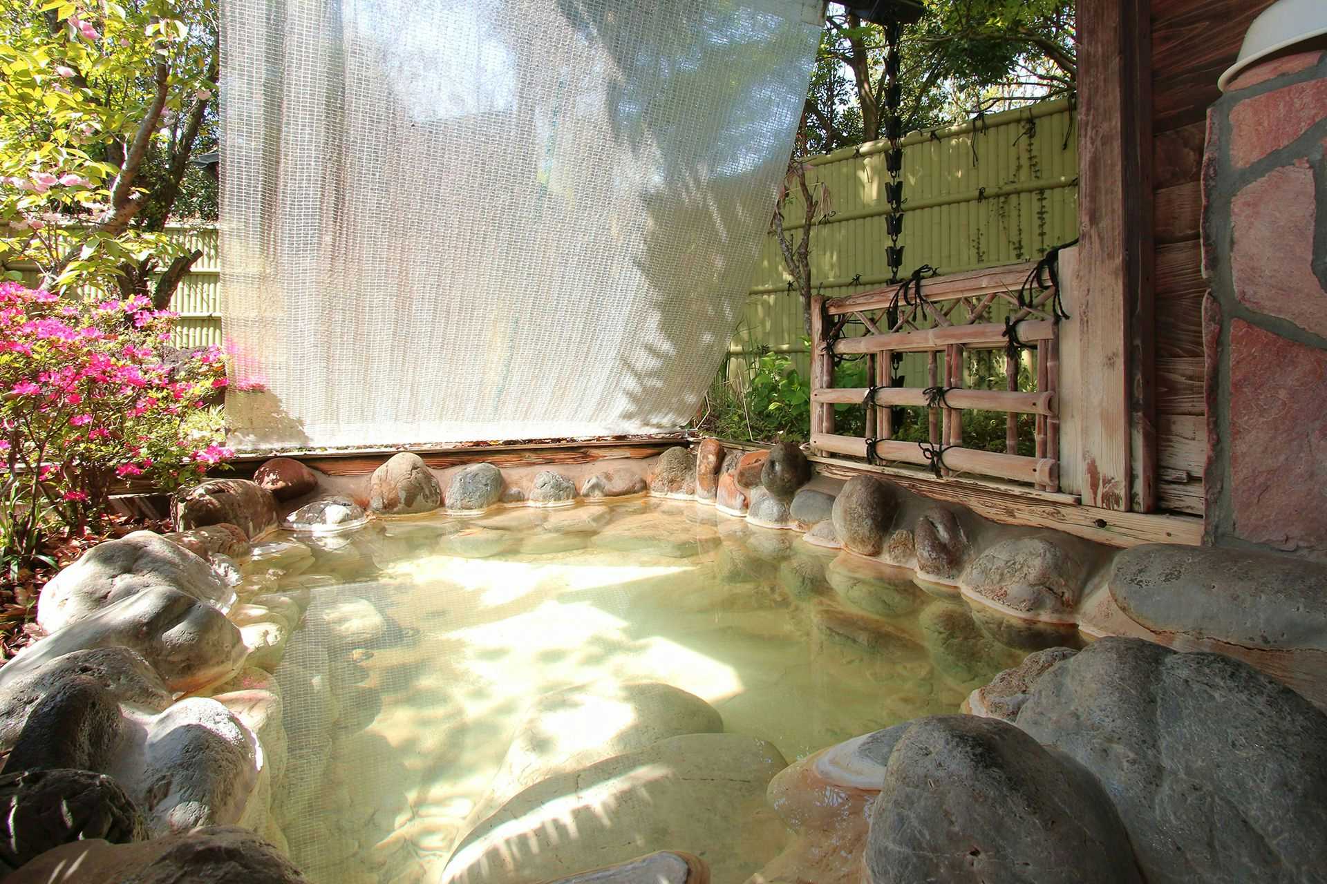 Jubei no Yado with an outdoor rock bath beside bamboo screening and garden plants.