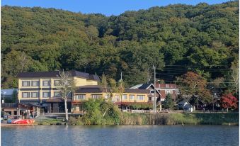 A row of buildings across the water beneath forested hills.