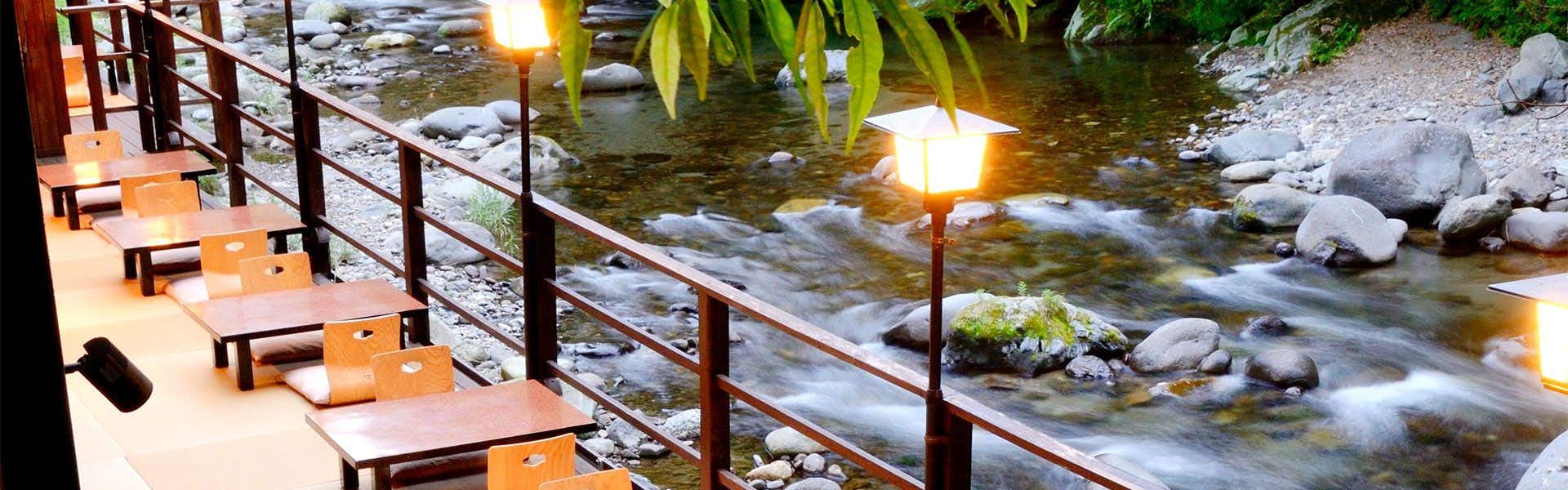 Mizu no Michi Kaze no Michi Yugashima Tatsuta wooden terrace with bench seating overlooks flowing stream lit by warm lanterns at night